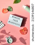 Small photo of Text Manage your menopause. Pink frame in hand. Menopause, hormone therapy concept. Estrogen replacement therapy awareness design. Pink background with exotic leaves, flowers, pills, estrogene gel.