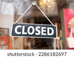 Small photo of a "closed" sign is attached with a suction cup to the glass of the entrance door of a fashion boutique