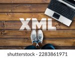 Small photo of Legs in sneakers standing next to laptop and XML on wooden floor. Extensible Markup Language