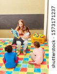 Small photo of Teacher or childminder and children reading from a children's book in a day care center