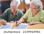 Small photo of Senior couple solving puzzles and maze game as memory training in the retirement home