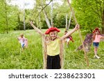 Small photo of Smiling girl with tricorn hat and stick standing arms outstretched in grass by friends
