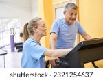 Small photo of Smiling young physiotherapist assisting elderly man to exercise on treadmill at rehabilitation center