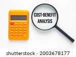 Small photo of Calculator and magnifying glass cost-benefit analysis. Cost-benefit analysis is a systematic process that businesses use to analyze which decisions either to proceed and to forgo.