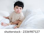 Small photo of Close-up portrait of sleepy baby after waking up sitting on the bed with soft white blanket, asian drowsy baby with copy space