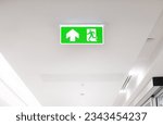 Lighted glowing green emergency exit signs in an office hallway with arrows pointing the way out of the building.