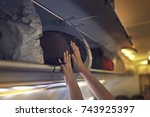 Passengers putting luggage into overhead locker on airplane. Hand putting luggage into panel overhead locker in airplane.
