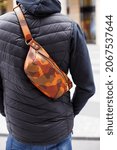 Small photo of A cropped beyond recognition man holding his new brown leather banana bag in the city. Men's Leather Hip Bag Over the Shoulder Waist Bag made of genuine leather. The man is standing with his back