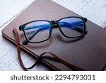 Small photo of black frame blue light blocking technology anti glare spectacles glasses on brown textured book wooden background