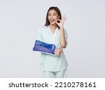 Small photo of Asian teenage woman wearing a patient gown put on a cast due to injury from an accident showing hand okay with an impressive smile.insurance concept.