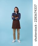 Small photo of Full length young asian man barista bartender employee in apron work in coffee shop hold hands crossed folded isolated on blue studio background. Small business startup concept