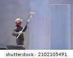 Small photo of Asian builder using long handle Roller brush to Painting Primer white color on Concrete Wall inside of house Construction Site