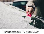 A woman is cleaning an icy window on a car with ice scraper. Focus on the ice scraper. Cold snowy and frosty morning.