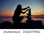 Silhouette of a woman balancing rocks and stones on the ocean sea coast at sunset sunrise time.