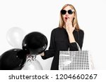 Elegant shocked girl, in black dress with sunglasses, with bags and black balls in her hands isolated on white background . Black Friday, shopping, discounts