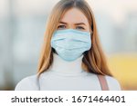 A young girl in the background of a building wears a face mask that protects against the spread of coronavirus disease. Close- up of a young woman with a surgical mask on her face against SARS-cov-2.