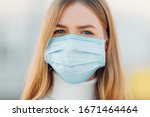 A young girl in the background of a building wears a face mask that protects against the spread of coronavirus disease. Close- up of a young woman with a surgical mask on her face against SARS-cov-2.