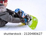 little boy sitting on snow putting his feet in snowboard bindings adjusting straps. High quality photo