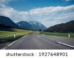 Asphalt road leading to the grip of the Austrian Alps. Color combination of road, lawn, sky and mountains. Perfect scenery of the Austrian landscape. Schladming road. Lowlands below Hoher Dachstein.