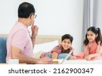 Small photo of Indian father working at home or apartment, raising hand to flaw, warn and ask for silence or quiet with blur background of children playing on bed. Family, Lifestyle, Business, Technology Concept