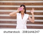 Small photo of Portrait of a Caucasian girl in white clothing with a flower in front of her eye, showing the okie sign with her hands on a brown ribbed background with copy space