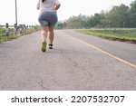 Rear view, low angle, wide shot with copy space of unrecognizable fat woman in sportswear running or jogging. Goal setting, weight loss, challenge, self-resolution concept.