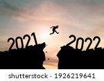 Welcome merry Christmas and happy new year in 2022,Silhouette Man jumping from 2021cliff to 2022 cliff with cloud sky and sunlight.