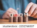 Businessman hand flipping wooden block cube from 2023 to 2024 on coins stacking for setup objective target business cost and budget planing of new year concept.