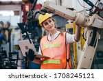 Female industrial engineer or technician worker in hard helmet and uniform using laptop checking on robotic arm machine. woman work hard in heavy technology invention industry manufacturing factory