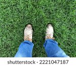 Top view of shoes in the feet of a man standing in grass. Concept of walking with tough wet shoes.