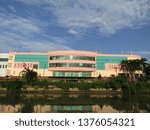 Small photo of Surabaya, Indonesia - April 21 2019: View of the back of JMP Grocery Mall Market Building with clear blue sky clouds and river background with trees around. Nearby with Red Bridge Historical Duct area