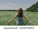 A woman enjoys the fresh air in nature in a green barley field. Summer countryside and gathering flowers. Atmospheric tranquil moment. Back view.