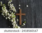 Small photo of Cross with flowers on a wooden background with the inscription Christ is Risen. Easter concept. Cross symbolizing the death and resurrection of Jesus Christ