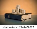 Small photo of A stack of coins with a Holy Bible Book in the background. The biblical concept of Christian offering, generosity, and giving tithes in church.
