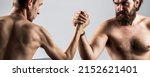 Small photo of Two man's hands clasped arm wrestling, strong and weak, unequal match. Arm wrestling. Heavily muscled bearded man arm wrestling a puny weak man. Arms wrestling thin hand, big strong arm in studio.