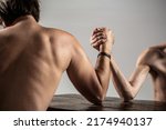 Small photo of Arm wrestling. Heavily muscled bearded man arm wrestling a puny weak man. Arms wrestling thin hand, big strong arm in studio. Two man's hands clasped arm wrestling, strong and weak, unequal match.