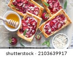 Delicious sweet sliced pies with strawberry. Puff pastry mini pies with strawberry, cream cheese, almond and honey. Top view.