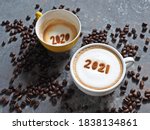 Goodbye 2020, Hello 2021 holidays food art theme coffee cups with number 2021 and 2020 on frothy surface flat lay on grey cement background with coffee beans. Holidays food art for Happy New Year.