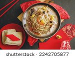 Small photo of Longevity noodle, Long life noodles or stir fried noodles served on dark background with uncooked dried noodles, red envelopes, ancient gold bullion nugget. Chinese Lunar New Year lucky food.