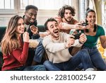 Small photo of Happy multi ethnic friends sitting on sofa playing video games - Cheerful generation z group having fun with modern technology videogames - Hobby and tech concept