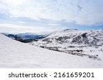 White snow-capped mountains in Norway over which there is a blue sky with soft puffy clouds
