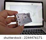 Small photo of Mechanical engineer hand holding CNC milled custom designed project in front of computer screen and drawings