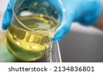 Small photo of Scientist hand wearing glove pouring petroleum yellow lubricating oil high viscosity into test tube in the laboratory. Automotive and industrial oil technology concept
