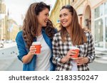 Outdoors portrait of two cheerful girls drinking coffee. Walking in the city.