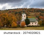 Small photo of The church in Brenna under a threatening autumn sky among plants with autumn leaves