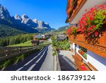 Road in alpine village with red flowers on house balcony, Colfosco, Dolomites Mountains, Italy