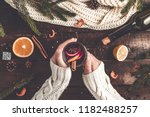 A young woman in a warm, knitted, white pullover is holding a Christmas, hot mulled wine in a glass with spices and citrus fruits. A cozy, winter evening. Winter drinks. Flat lay, top view 
