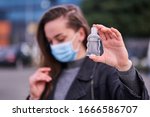 Woman in medical protective mask with an antibacterial antiseptic gel for hands disinfection outdoors. Health protection prevention during flu virus outbreak and coronavirus epidemic