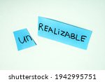 Small photo of Scissors cutting paper with word UNREALIZABLE on blue background. Concept