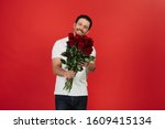 Handsome wearing white T-shirt, holding bouquet with red roses on red background. Celebrating Happy Valentine`s day